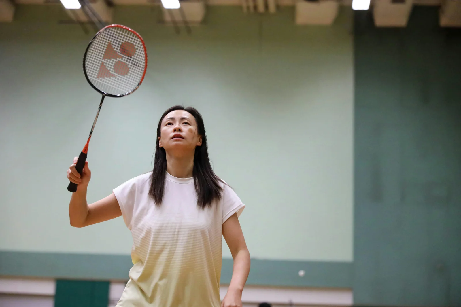 Badminton player serving with Yonex racket looking upward on indoor court