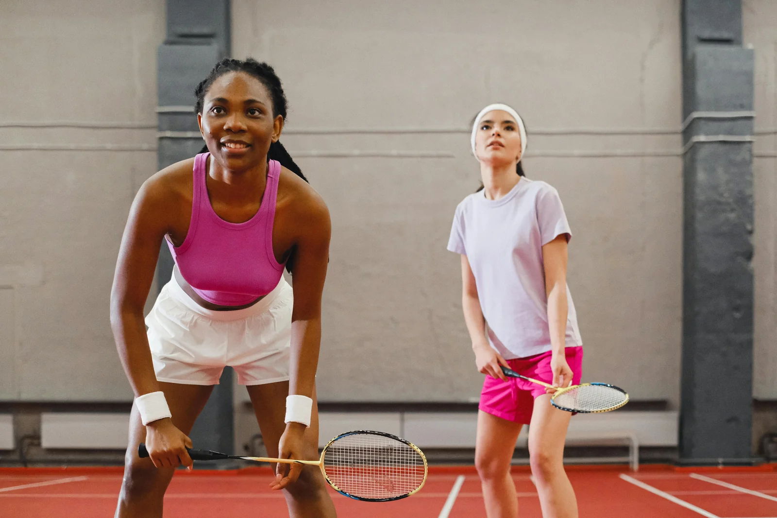 Two badminton doubles players in ready stance on indoor court showing partnership formation