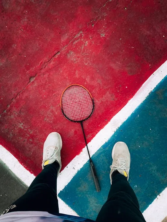Player standing at junction of multicolored badminton court surfaces — aggregate win rate hides venue-specific patterns