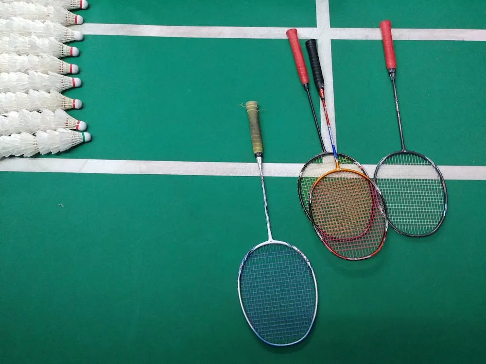 Multiple badminton rackets and shuttlecocks on Asian tournament court surface — geographic performance patterns BWF World Tour