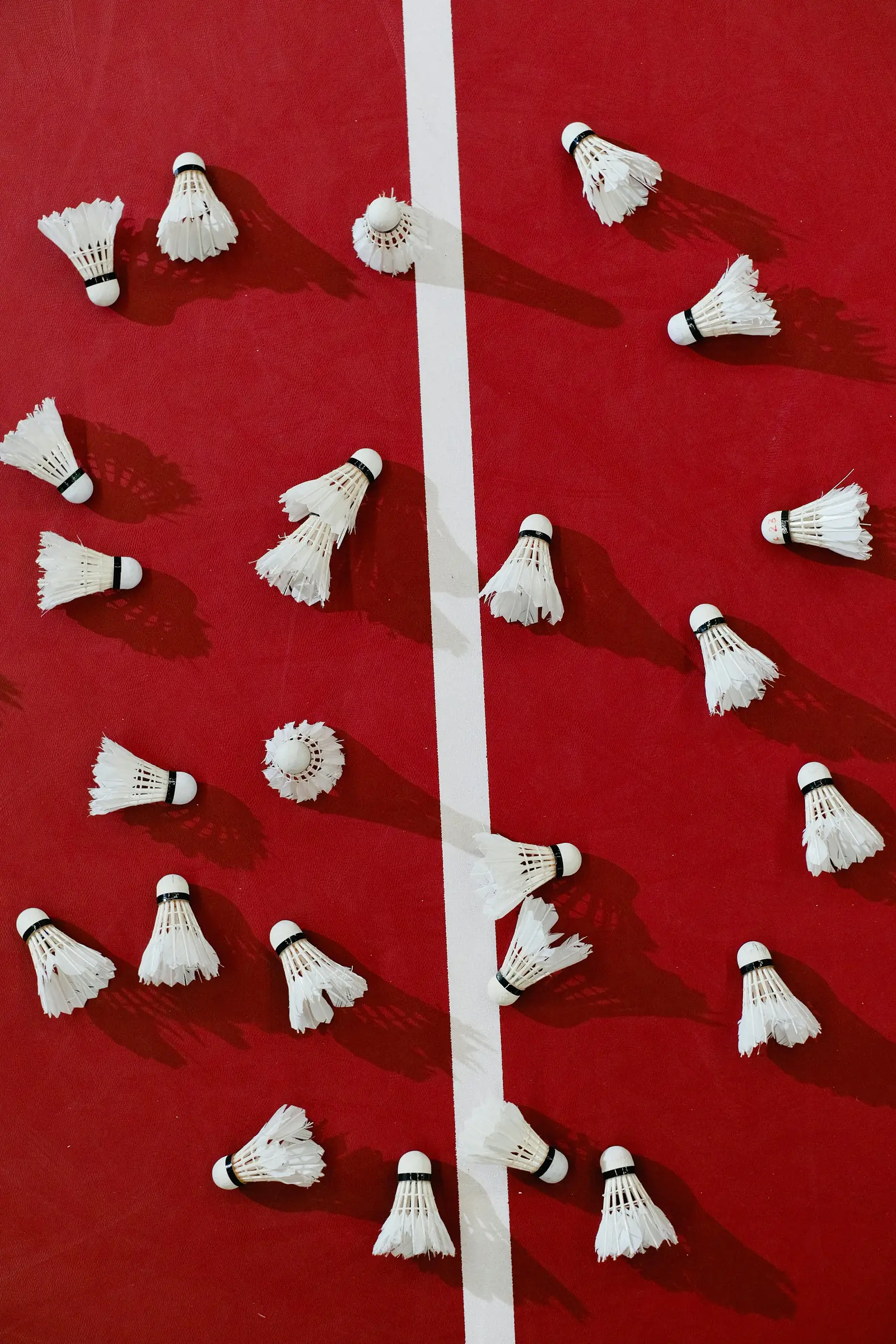 Multiple badminton shuttlecocks arranged on red court aerial view