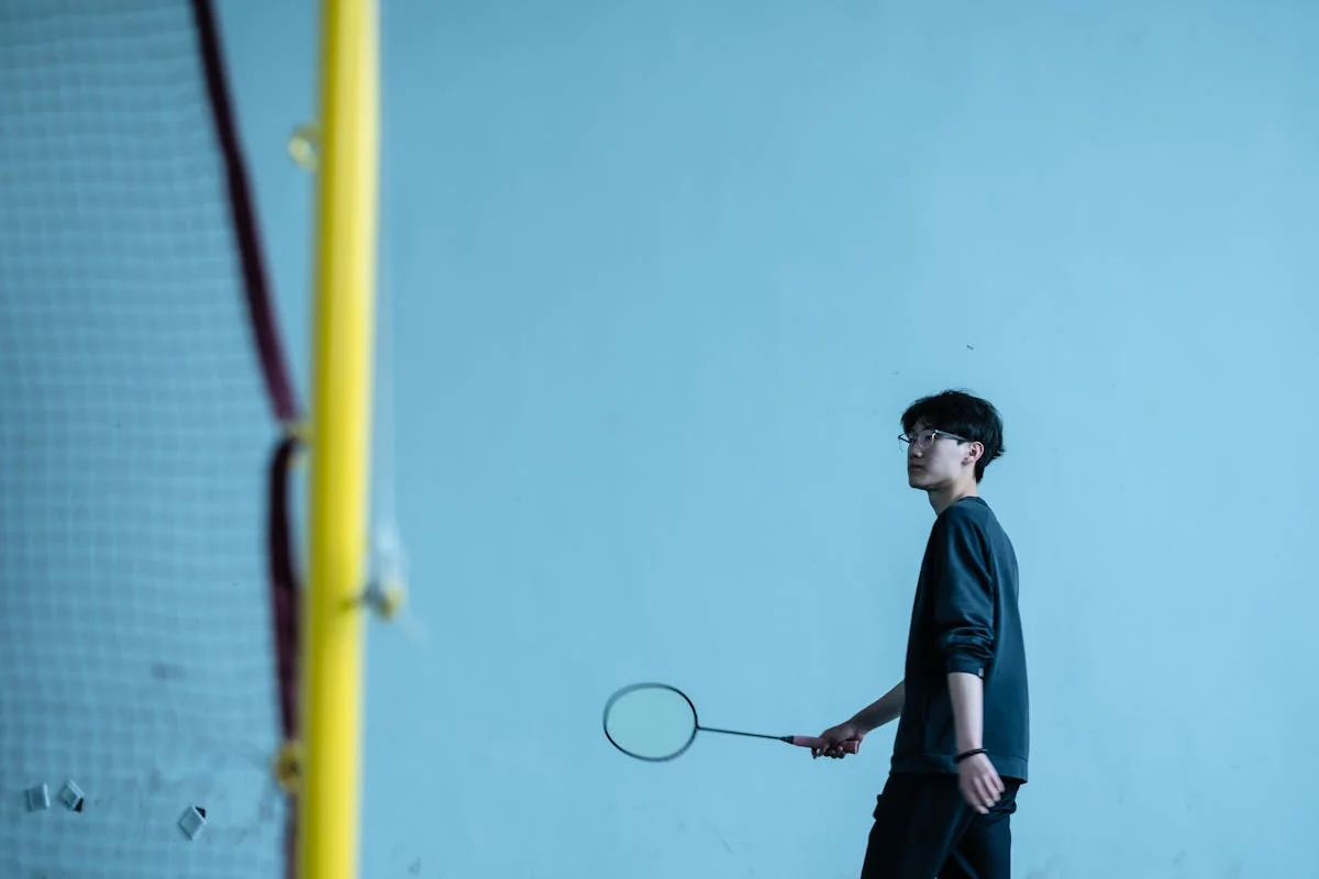 Badminton player standing near the net with racket during indoor competition