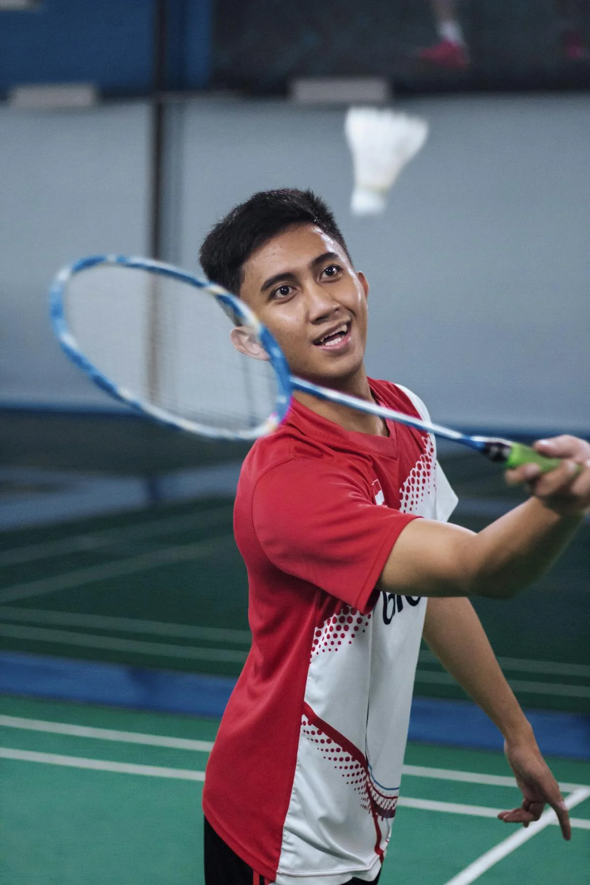 Male badminton player mid-smash with shuttlecock visible above racket during indoor match