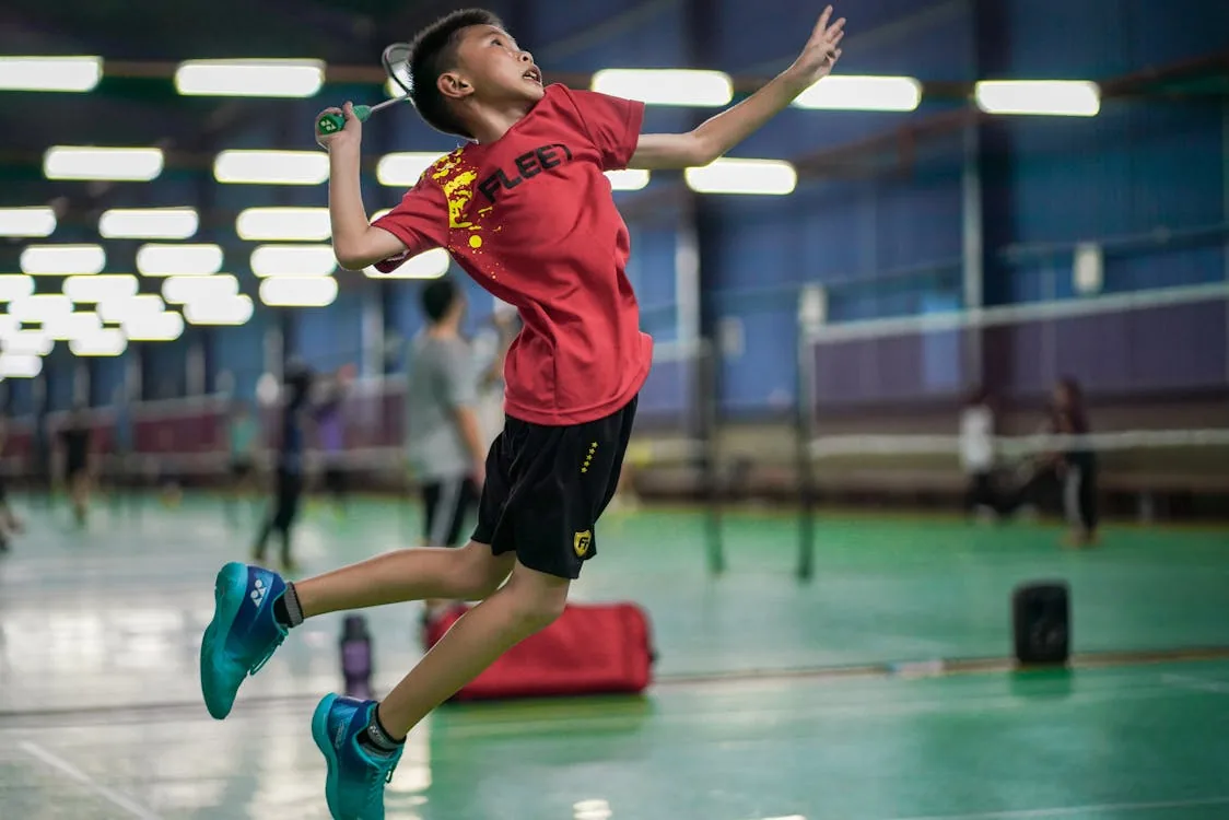 Young badminton player jumping to strike shuttlecock in indoor sports hall — what finals reached reveals in career data
