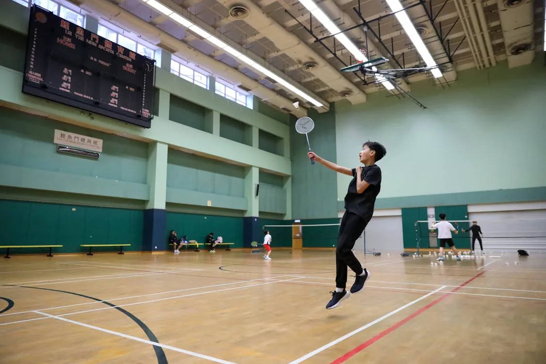 Badminton player mid-jump shot at indoor sports centre with scoreboard — Lee Chong Wei vs Lin Dan era finals comparison
