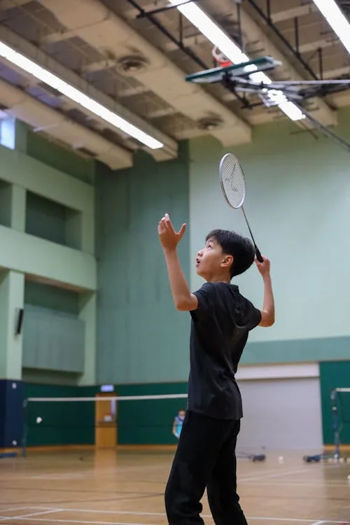 Badminton player preparing service action at indoor green court — modern BWF World Tour finals and titles evaluation