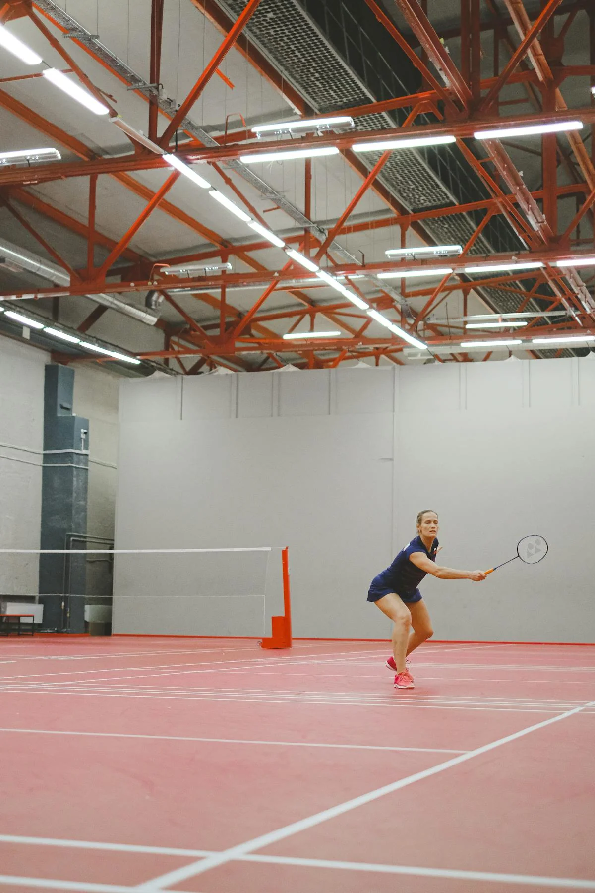 Badminton player sprinting to return a shot on a large indoor court with the full court visible