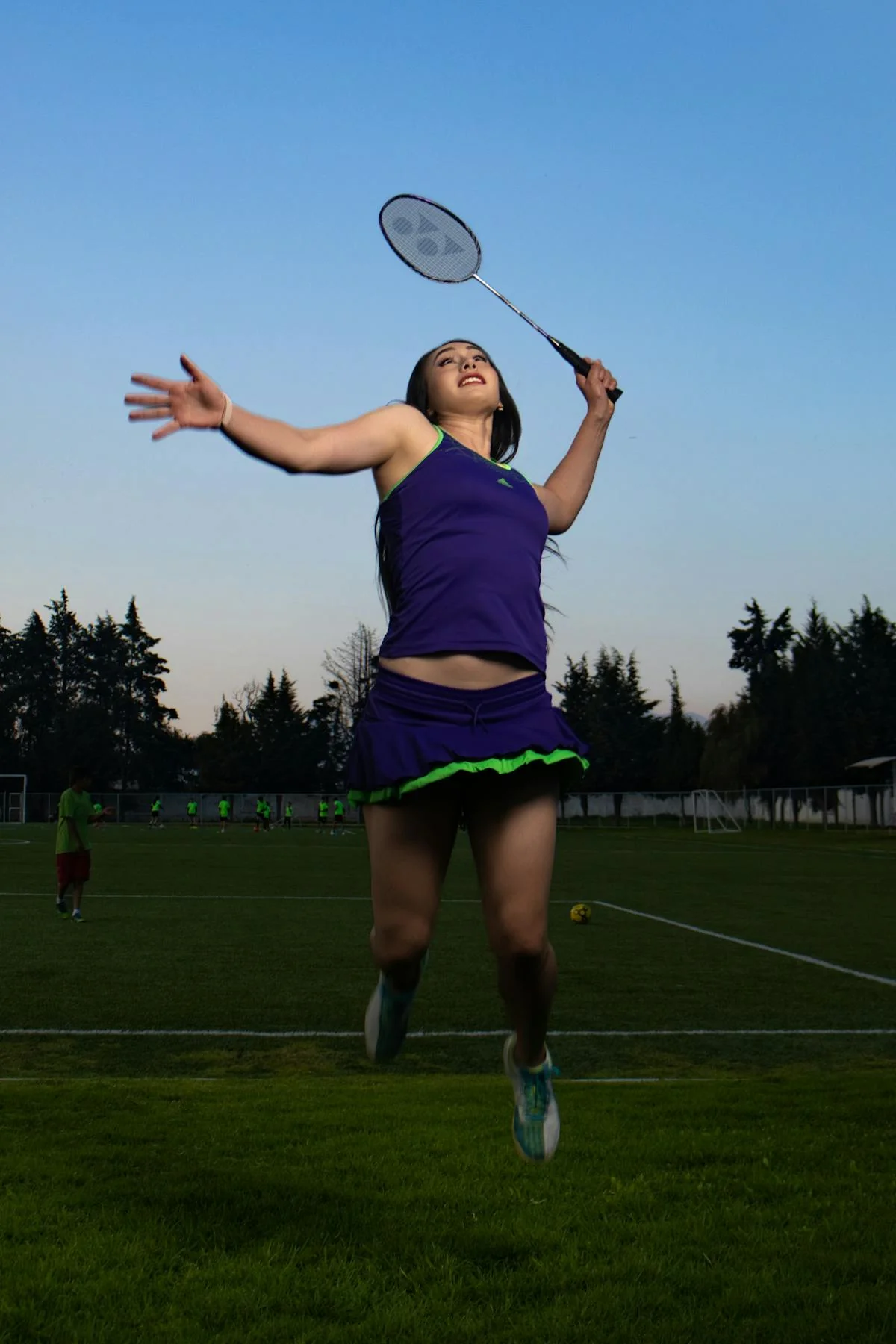 Badminton player executing a powerful jump smash on outdoor court at sunset