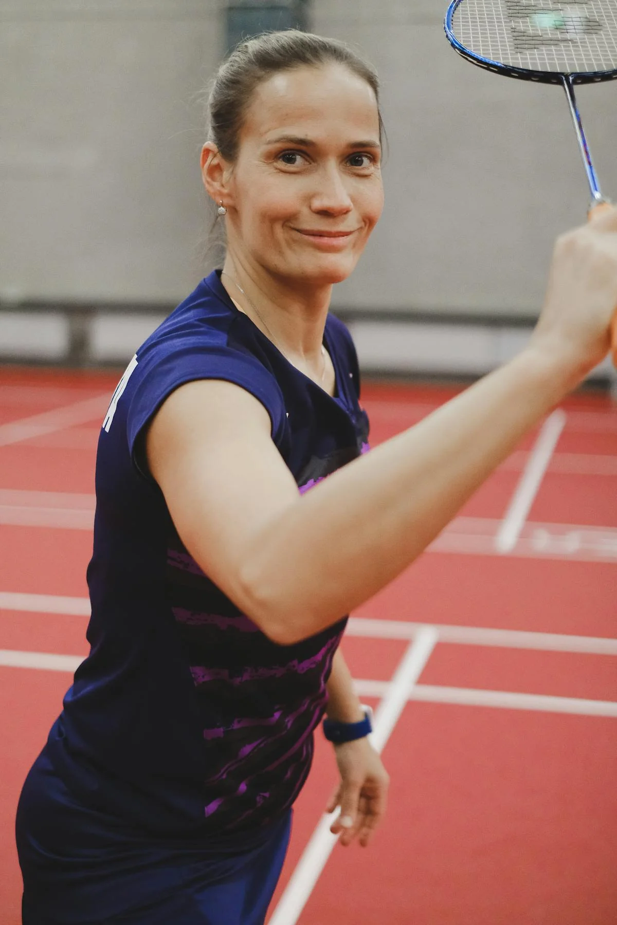 Badminton player on indoor red court with focused expression during competitive play