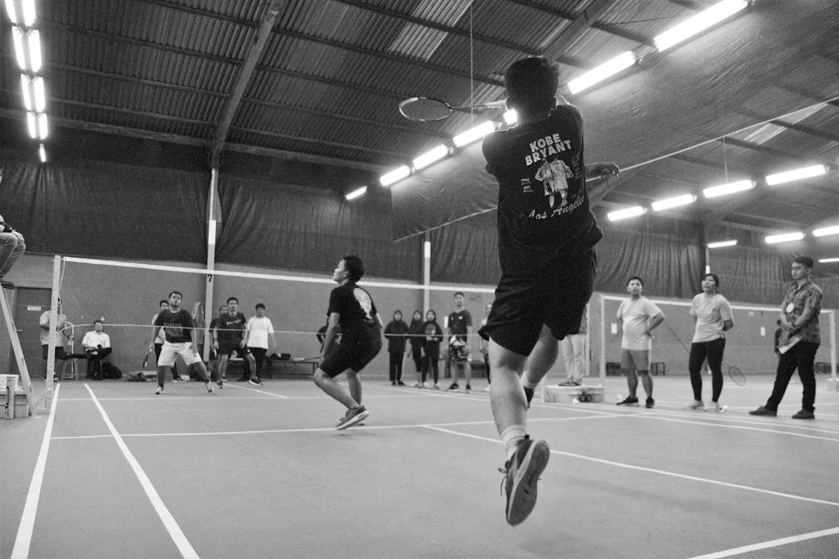Black and white photograph of two badminton players competing indoors with spectators and officials observing