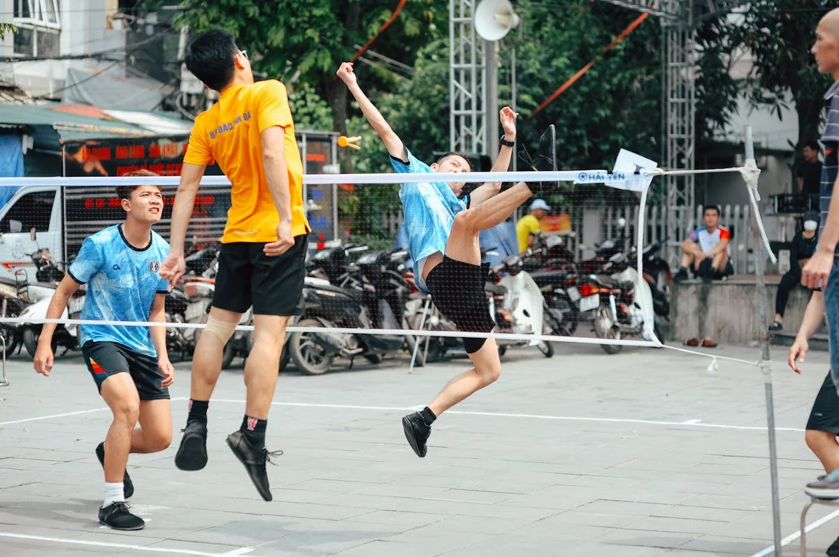 Badminton player executing a powerful jump smash over the net at an outdoor competition with teammates watching